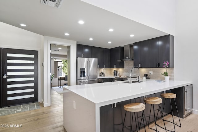 kitchen featuring a breakfast bar area, light wood-type flooring, kitchen peninsula, high quality fridge, and sink