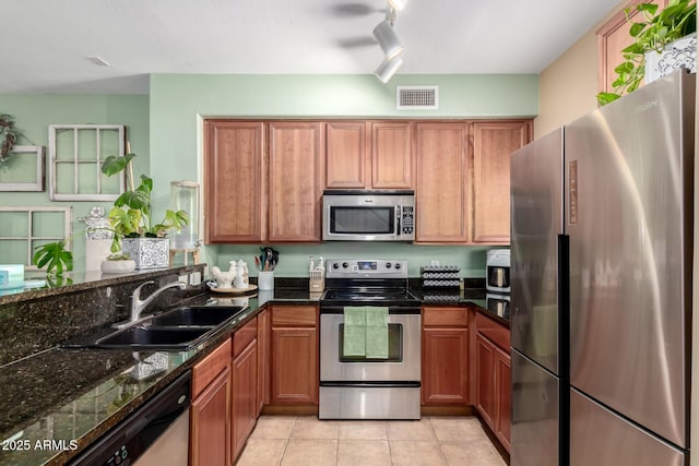 4072 E Windsor Dr, Gilbert, AZ 85296 - kitchen with appliances with stainless steel finishes, brown cabinets, track lighting, light tile patterned floors, and dark stone counters