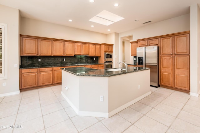 kitchen with stainless steel appliances, brown cabinets, a sink, and a center island with sink