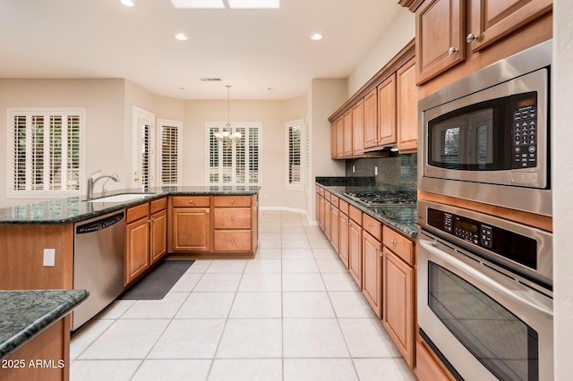 kitchen with light tile patterned floors, tasteful backsplash, appliances with stainless steel finishes, a sink, and dark stone counters