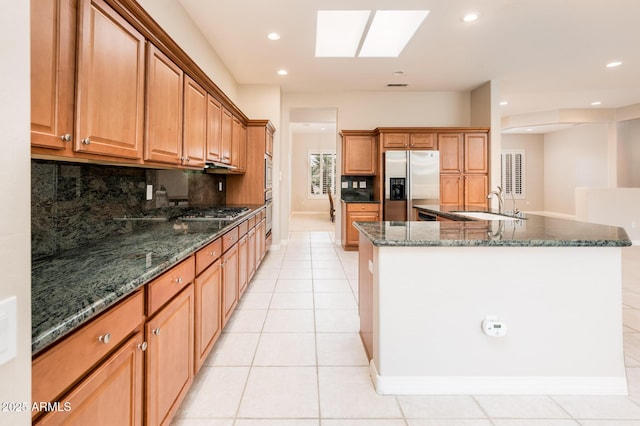 kitchen with stainless steel appliances, a skylight, a sink, a large island, and tasteful backsplash