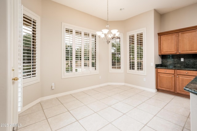 unfurnished dining area featuring light tile patterned floors, baseboards, and a notable chandelier