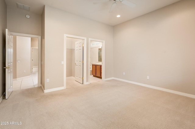 unfurnished bedroom featuring a walk in closet, recessed lighting, light colored carpet, ensuite bath, and baseboards