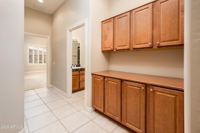 corridor with light tile patterned floors, baseboards, and a sink