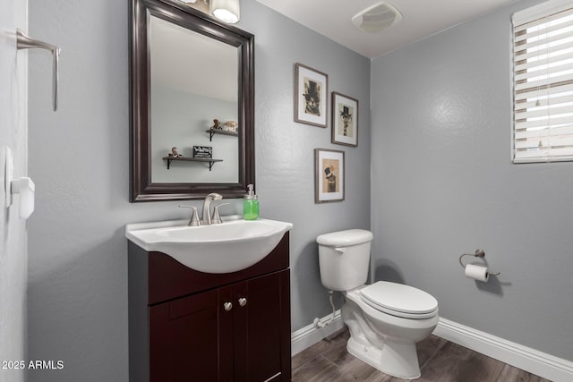half bathroom with toilet, vanity, baseboards, and wood finished floors