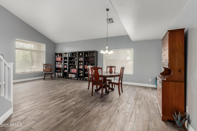 dining area with a wealth of natural light, vaulted ceiling, a chandelier, and light wood finished floors