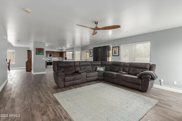 living room with a wealth of natural light, ceiling fan, baseboards, and dark wood-style floors