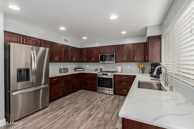 kitchen with light stone counters, a sink, light wood finished floors, stainless steel appliances, and visible vents