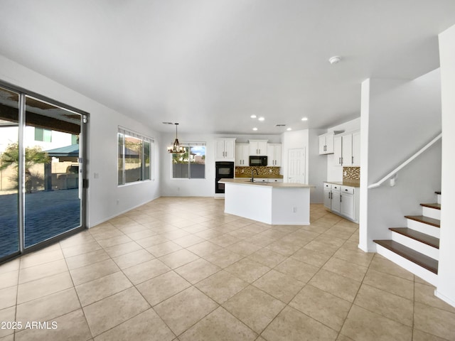 kitchen with tasteful backsplash, white cabinets, a kitchen island with sink, light tile patterned floors, and black appliances