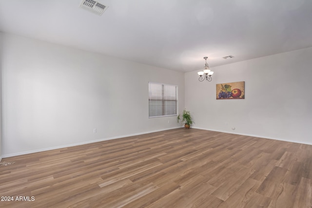 empty room featuring wood-type flooring and a chandelier