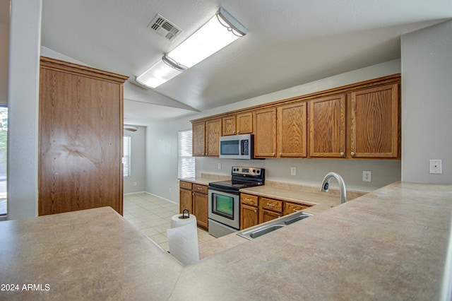 kitchen with appliances with stainless steel finishes, sink, vaulted ceiling, and light tile patterned flooring