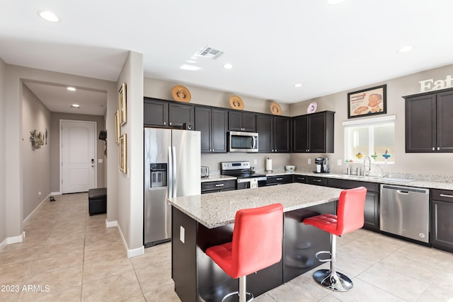 kitchen featuring appliances with stainless steel finishes, light tile patterned flooring, light stone countertops, a kitchen island, and a breakfast bar