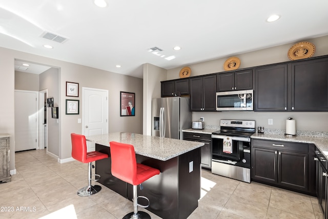 kitchen with a kitchen island, stainless steel appliances, light tile patterned flooring, light stone counters, and a breakfast bar area