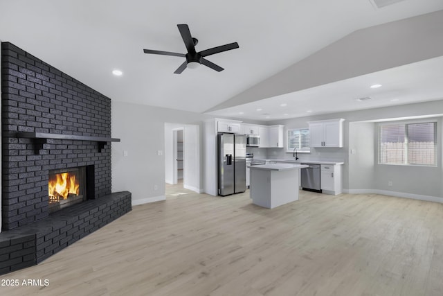 unfurnished living room with lofted ceiling, a fireplace, light hardwood / wood-style flooring, and plenty of natural light