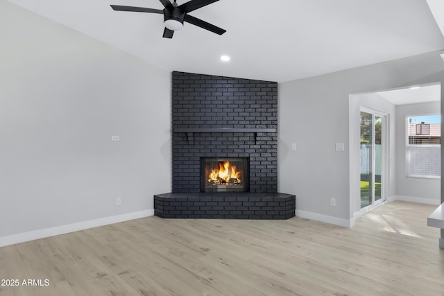 unfurnished living room featuring lofted ceiling, a fireplace, light wood-type flooring, and ceiling fan