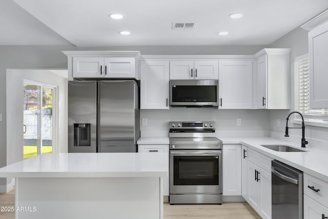 kitchen with appliances with stainless steel finishes, white cabinetry, light wood-type flooring, and sink