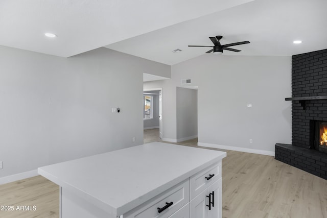 kitchen with white cabinetry, a fireplace, ceiling fan, light wood-type flooring, and a kitchen island