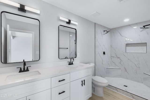 bathroom with toilet, hardwood / wood-style floors, tiled shower, and vanity