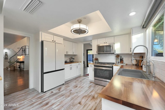 kitchen featuring sink, light hardwood / wood-style flooring, appliances with stainless steel finishes, a tray ceiling, and white cabinetry