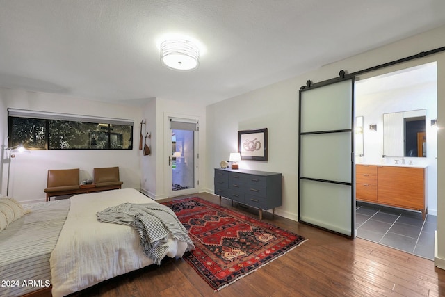 bedroom featuring connected bathroom, dark hardwood / wood-style floors, a barn door, and sink