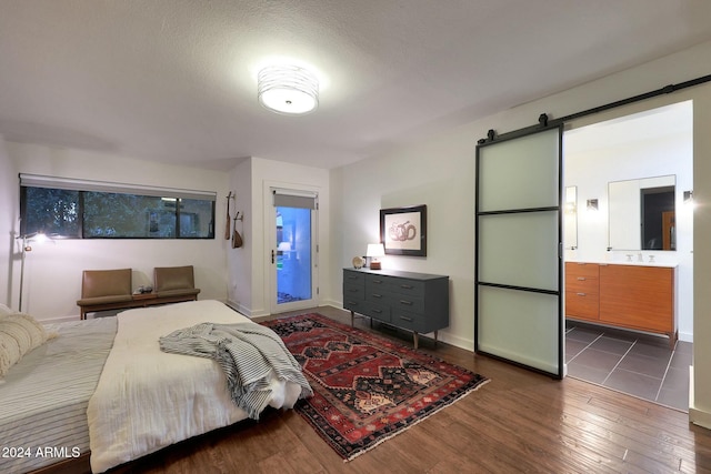 bedroom with dark hardwood / wood-style floors, a barn door, and ensuite bath