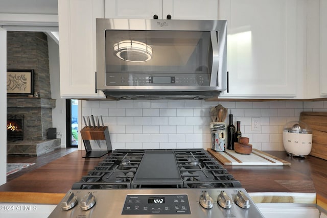 kitchen featuring a stone fireplace, white cabinetry, and tasteful backsplash