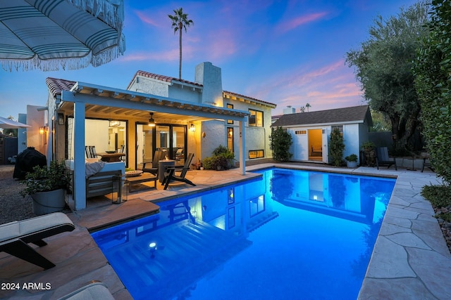 pool at dusk featuring an outbuilding, an outdoor living space, ceiling fan, and a patio area