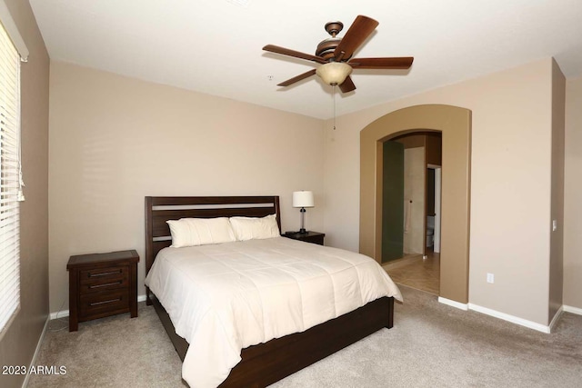 carpeted bedroom with arched walkways, ceiling fan, and baseboards