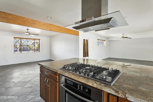 kitchen with oven, stainless steel gas cooktop, beamed ceiling, ceiling fan, and island range hood