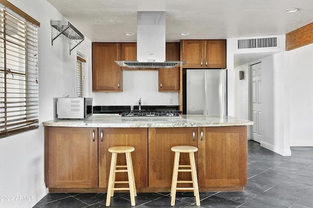 kitchen with island exhaust hood, a breakfast bar area, stainless steel appliances, kitchen peninsula, and light stone counters