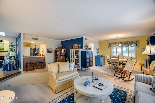 living room featuring a brick fireplace, crown molding, a chandelier, and light wood-type flooring