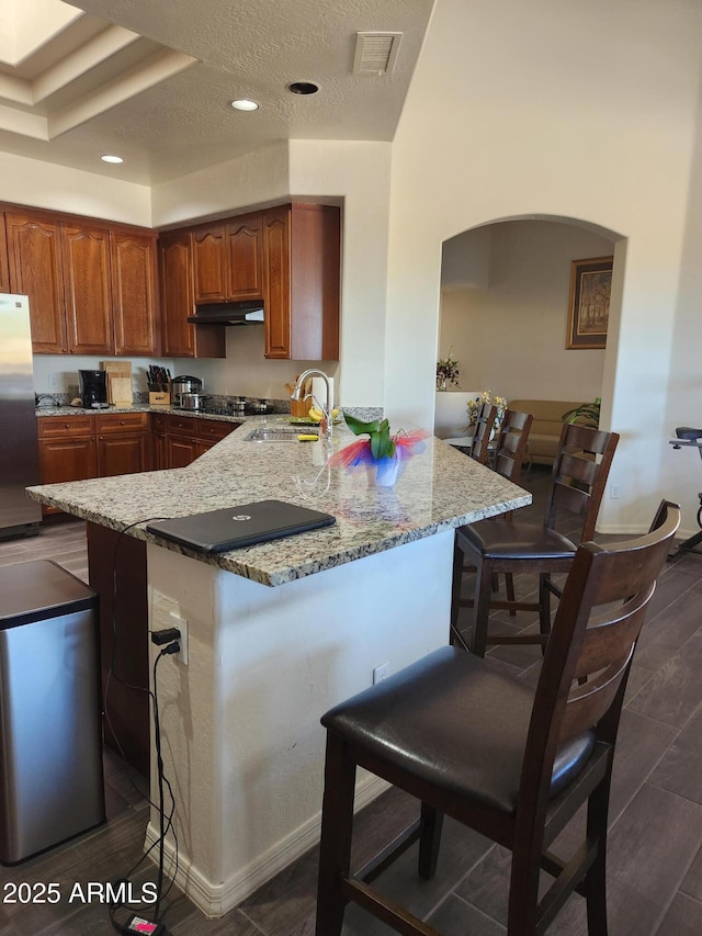 kitchen with a breakfast bar, stainless steel refrigerator, sink, kitchen peninsula, and light stone countertops