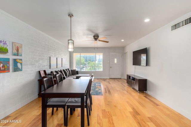 dining space with ceiling fan, crown molding, light hardwood / wood-style floors, and brick wall