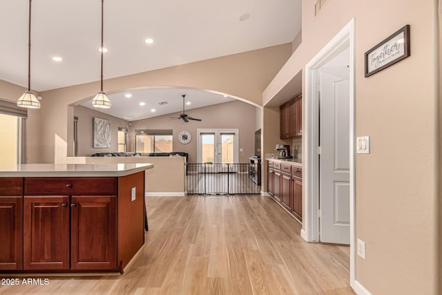 kitchen with arched walkways, lofted ceiling, decorative light fixtures, light countertops, and light wood-style floors