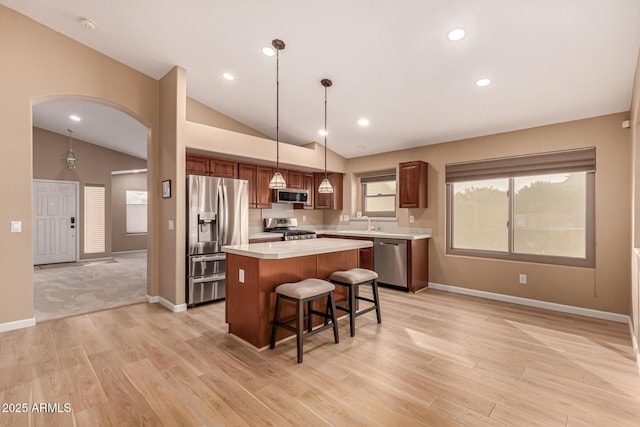 kitchen with a center island, arched walkways, stainless steel appliances, light countertops, and vaulted ceiling