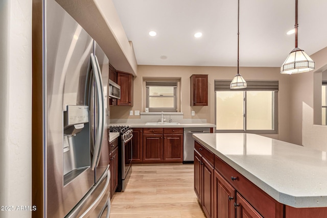 kitchen featuring light wood-style flooring, recessed lighting, stainless steel appliances, a sink, and hanging light fixtures