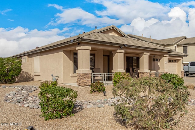 view of front facade with a tile roof, stucco siding, a porch, an attached garage, and stone siding