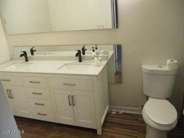 bathroom with double vanity, baseboards, toilet, and a sink