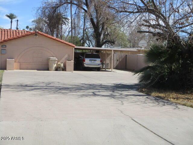 exterior space featuring concrete driveway, a carport, a tile roof, and stucco siding