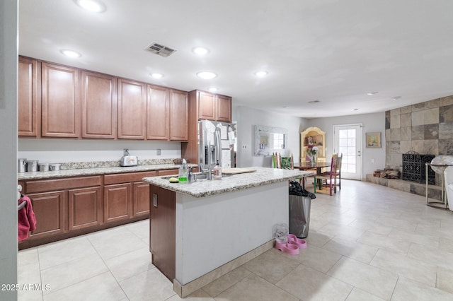 kitchen featuring light stone counters, recessed lighting, visible vents, stainless steel refrigerator with ice dispenser, and an island with sink