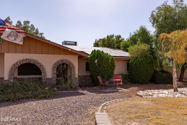 view of front of home with stone siding, roof mounted solar panels, and a patio