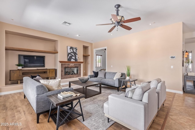 living room featuring ceiling fan, a high end fireplace, built in features, and light hardwood / wood-style floors