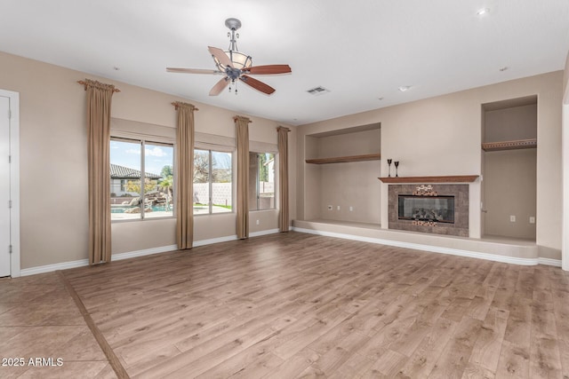 unfurnished living room with ceiling fan, built in shelves, and light wood-type flooring