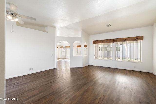 empty room featuring baseboards, visible vents, a ceiling fan, arched walkways, and dark wood-type flooring