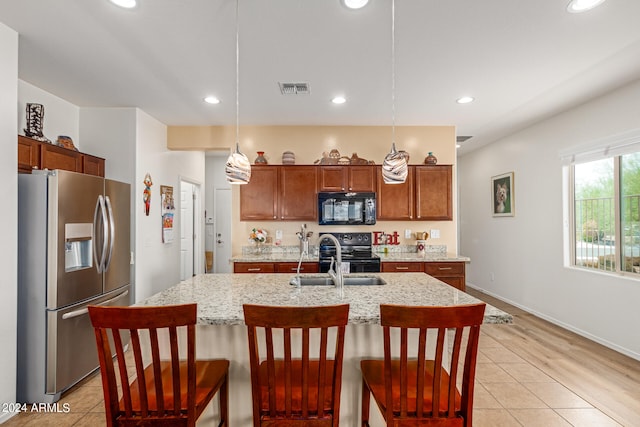 kitchen with decorative light fixtures, light hardwood / wood-style floors, black appliances, an island with sink, and a kitchen bar