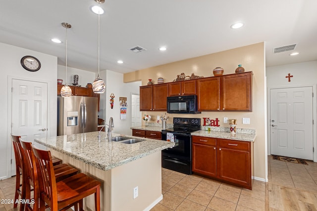 kitchen featuring pendant lighting, black appliances, light stone counters, sink, and a center island with sink