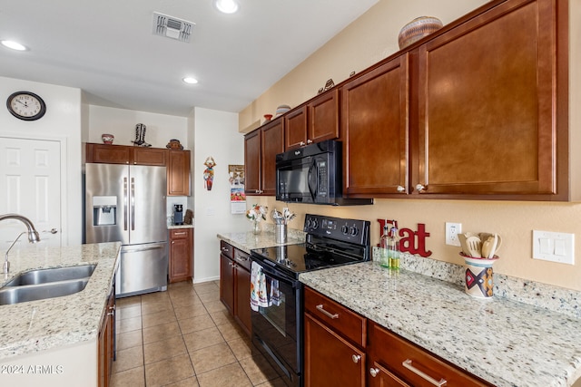 kitchen with light tile patterned floors, black appliances, an island with sink, sink, and light stone countertops