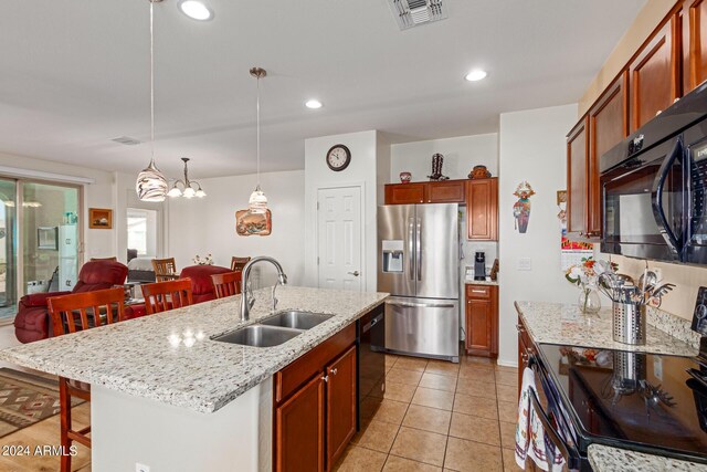 kitchen featuring light stone counters, sink, black appliances, pendant lighting, and a kitchen island with sink