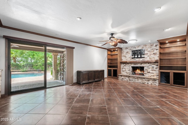 unfurnished living room with built in features, tile patterned floors, a ceiling fan, a fireplace, and crown molding