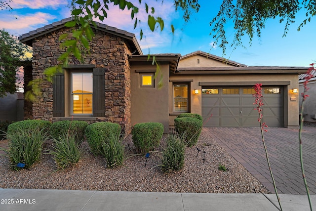 view of front of property featuring a garage, stucco siding, decorative driveway, and stone siding